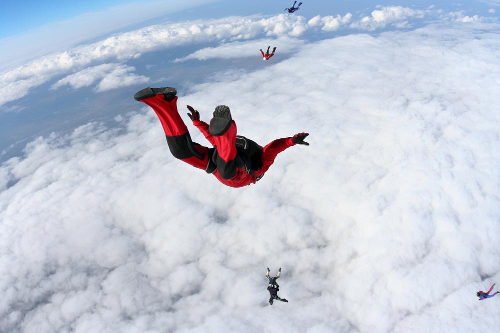Skydiver speeding down to earth above clouds
